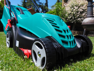 A bright turquoise lawnmower on a lush green lawn, set against a sunny backdrop of trees and bushes, creates a vibrant and lively garden scene.