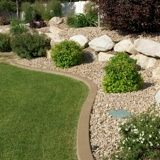 Alt text: "A well-manicured garden featuring a curved border separating lush green grass from a gravel area with scattered bushes and large rocks."